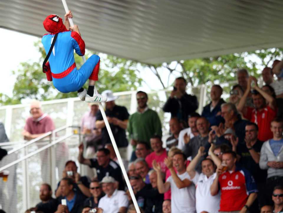 A fan dressed in a Spiderman costume climbs up a stand support