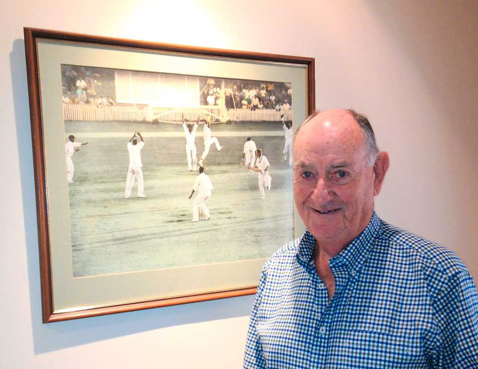 Ian Meckiff poses next to the picture of the tied Test at home