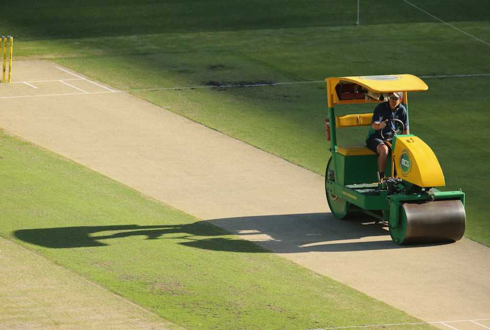A groundsman runs a roller on the pitch