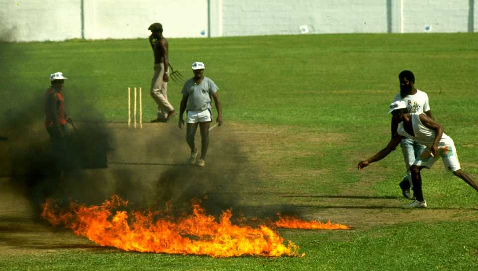 Ground staff set parts of the pitch alight to dry out damp areas before a tour match between Windward Islands and England, St Lucia, February 1990