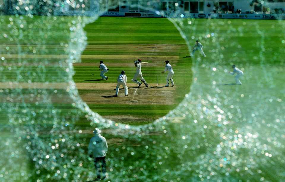 Mal Loye hits a boundary as seen through the hole in the press box window that he created with an earlier six
