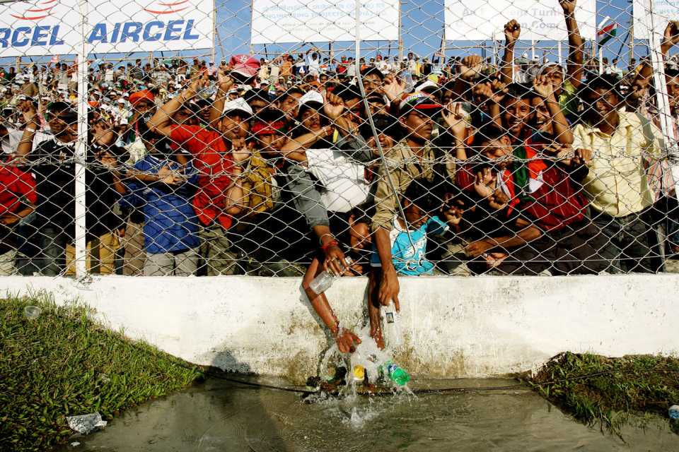 Spectators struggle to take water from a tap on the other side of the fencing
