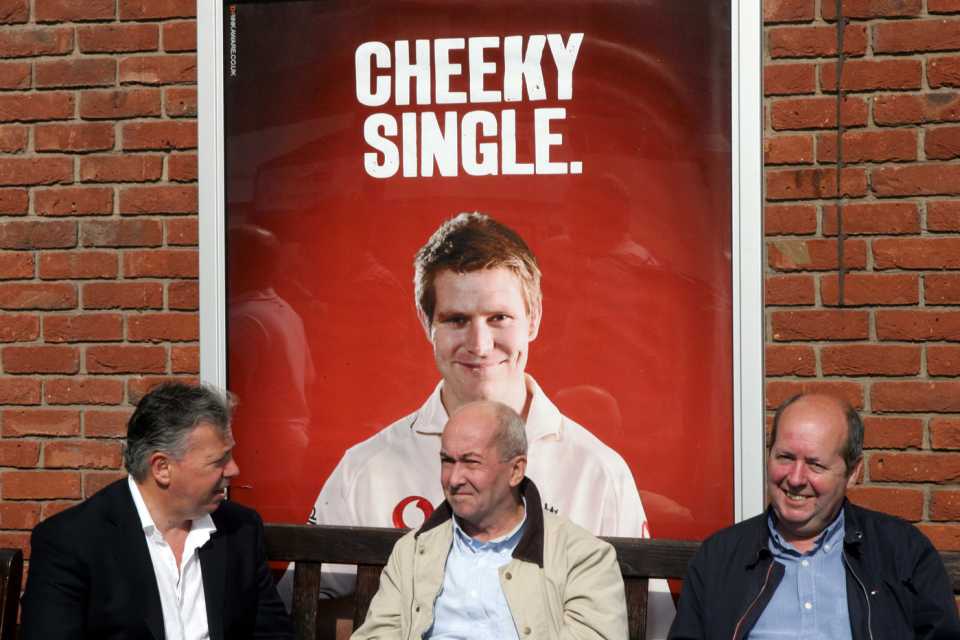 Three spectators sit in front of a Matthew Hoggard poster