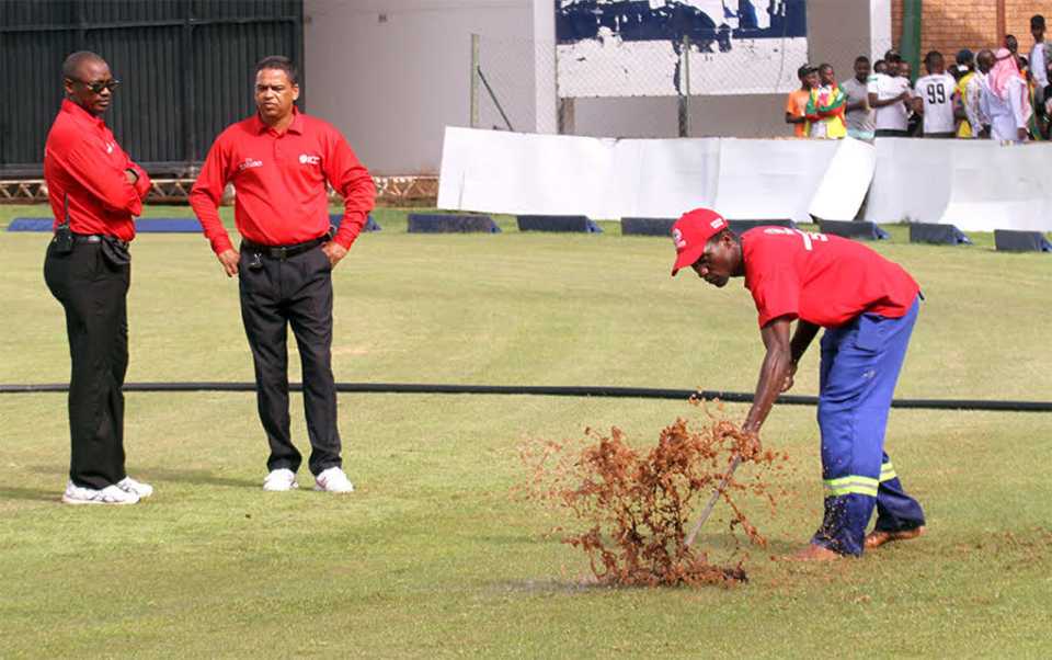 Umpires Jeremiah Matibiri and Shaun George watch ground staff attempt to dry the outfield