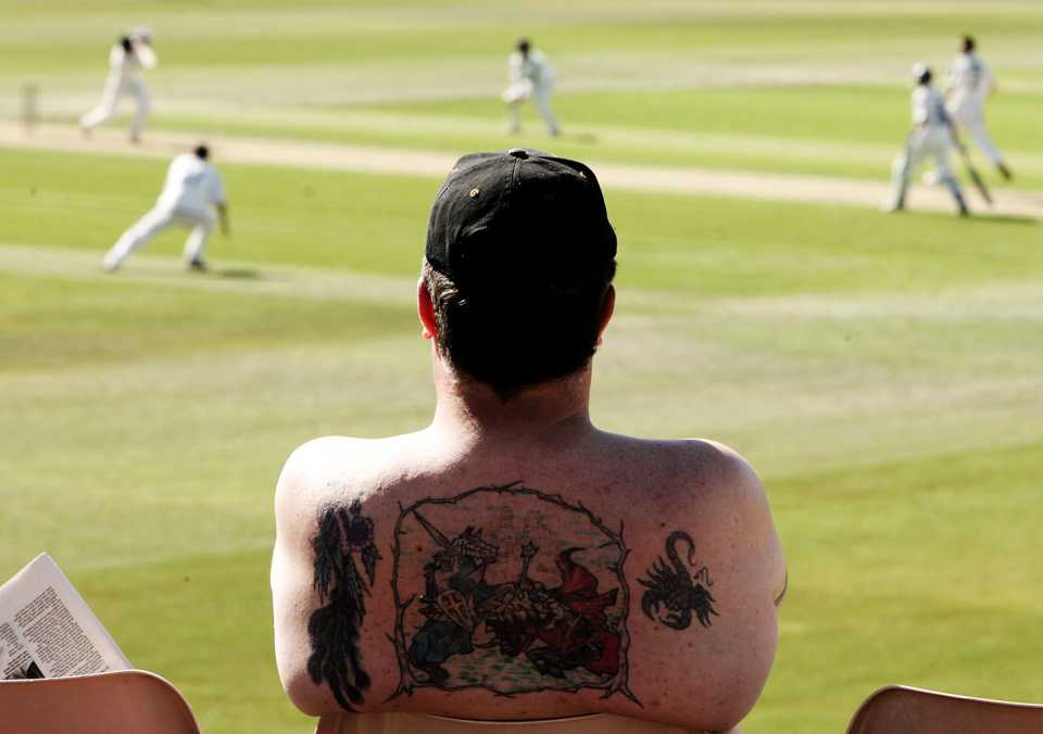 A spectator with a back tattoo watches a county game