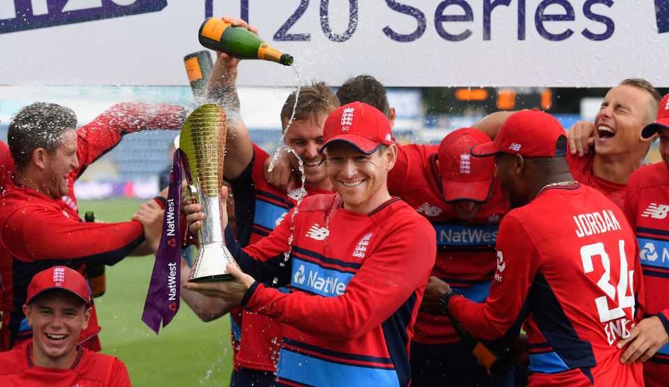 Eoin Morgan lifts the series trophy as the champagne corks pop in the background