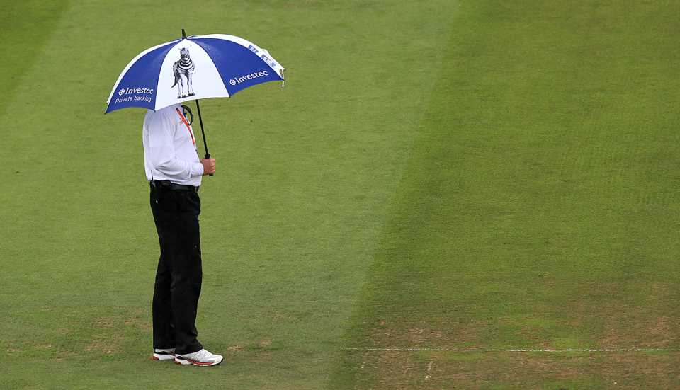 An umpire stands under an umbrella during a rain interruption