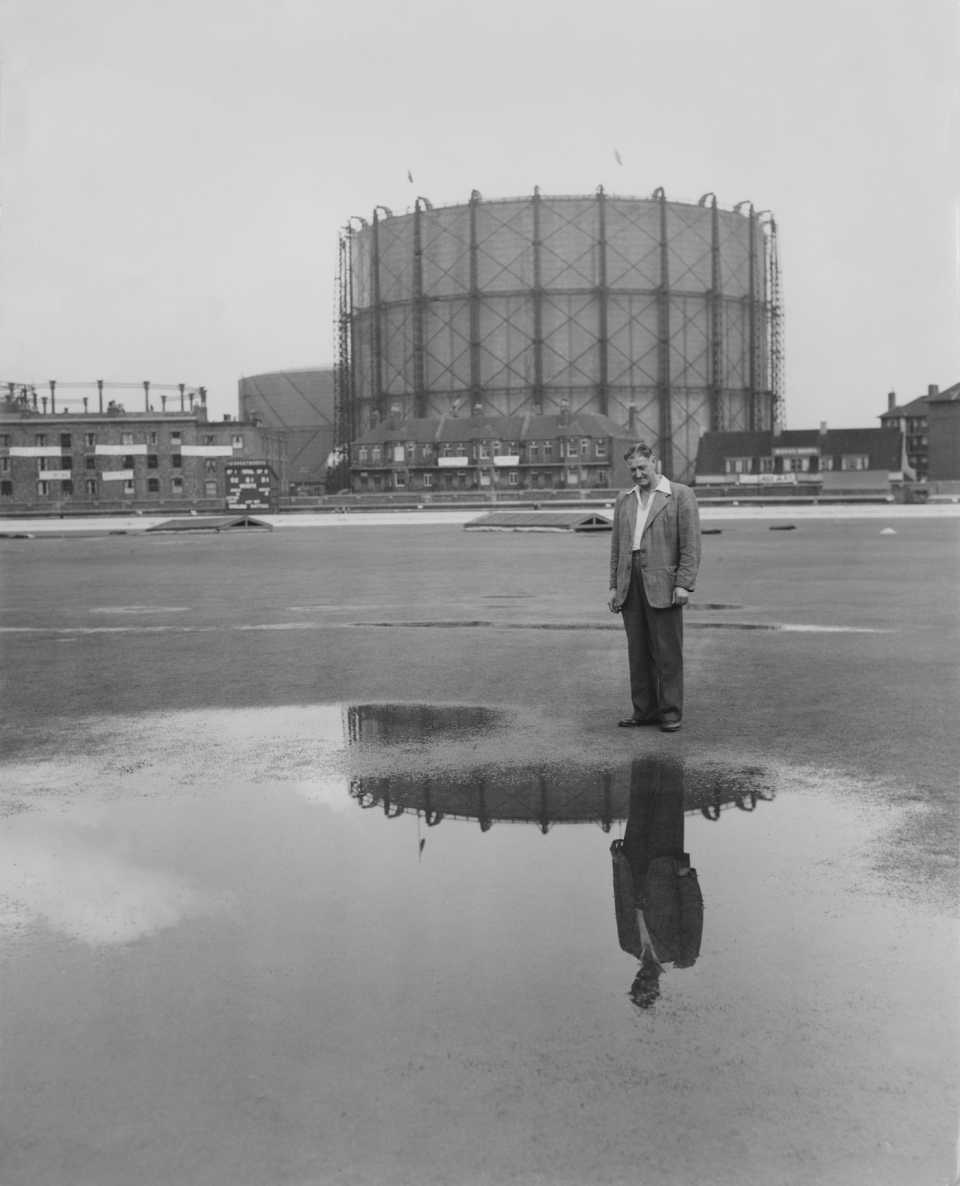 Oval head groundsman Bert Lock examines a pool of water in the outfield, as bad weather and rain postpones play