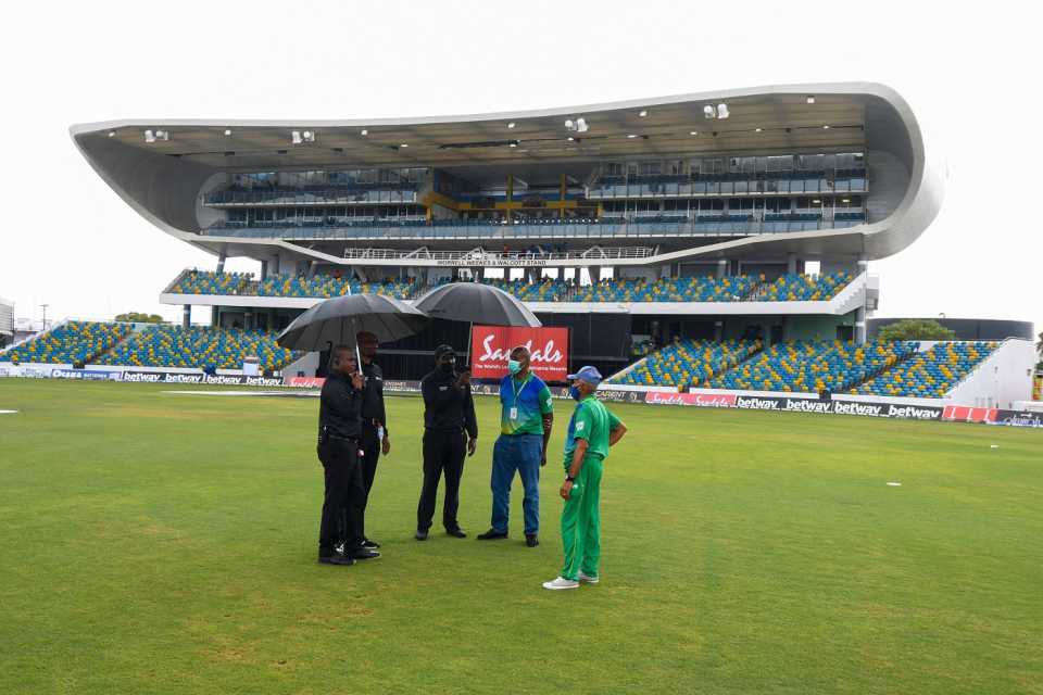 The umpires and the ground staff take shelter under an umbrella while waiting for the rain to clear 