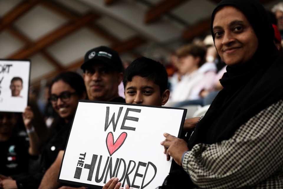 Spectators hold up a "We love the Hundred" sign