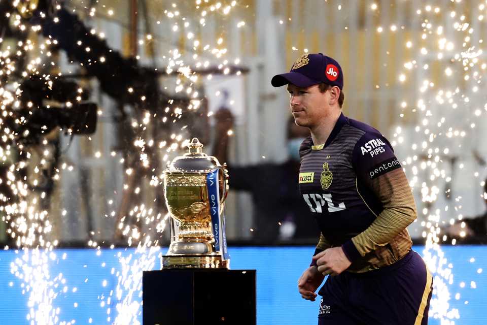 Eoin Morgan runs onto the ground past the IPL trophy