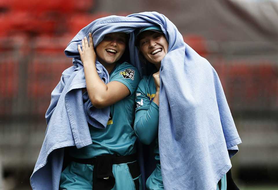 Amelia Kerr and Maddy Green share a laugh and keep warm during a rain delay