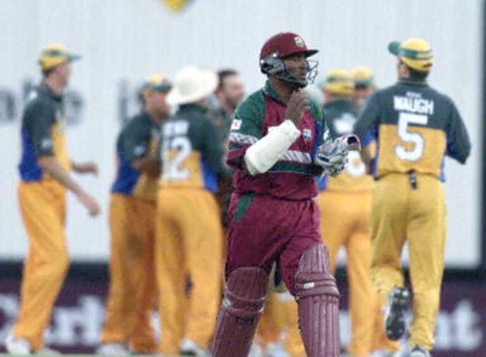 West Indies batsman Brian Lara walks dejected as the Australian team celebrate at the first Final of the Tri Nations series in Sydney 07 February 2001. Lara made seven boundarys from 38 balls before being caught by Australian wicket-keeper Adam Gilchrist off the bowling of Damien Fleming as the West Indies chased the Australian total of 254.
