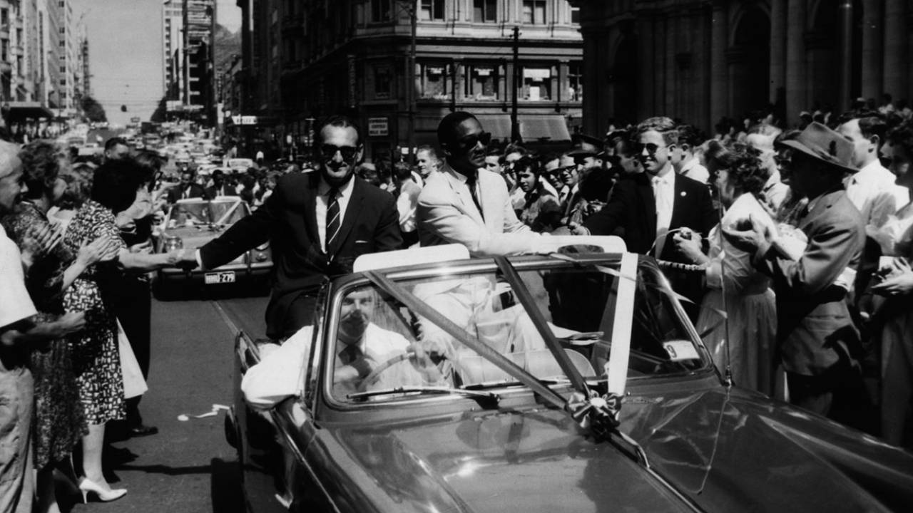 Gerry Gomez and Frank Worrell sit in an open-top car and drive through the streets of Melbourne greeting fans who came to see off the West Indies side at the end of the tour, February 20, 1961