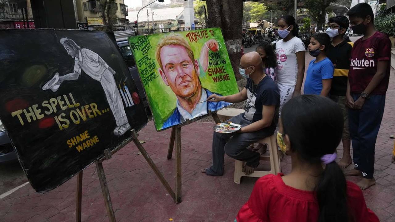Onlookers watch an artist work on a Shane Warne painting on a Mumbai sidewalk, March 5, 2022