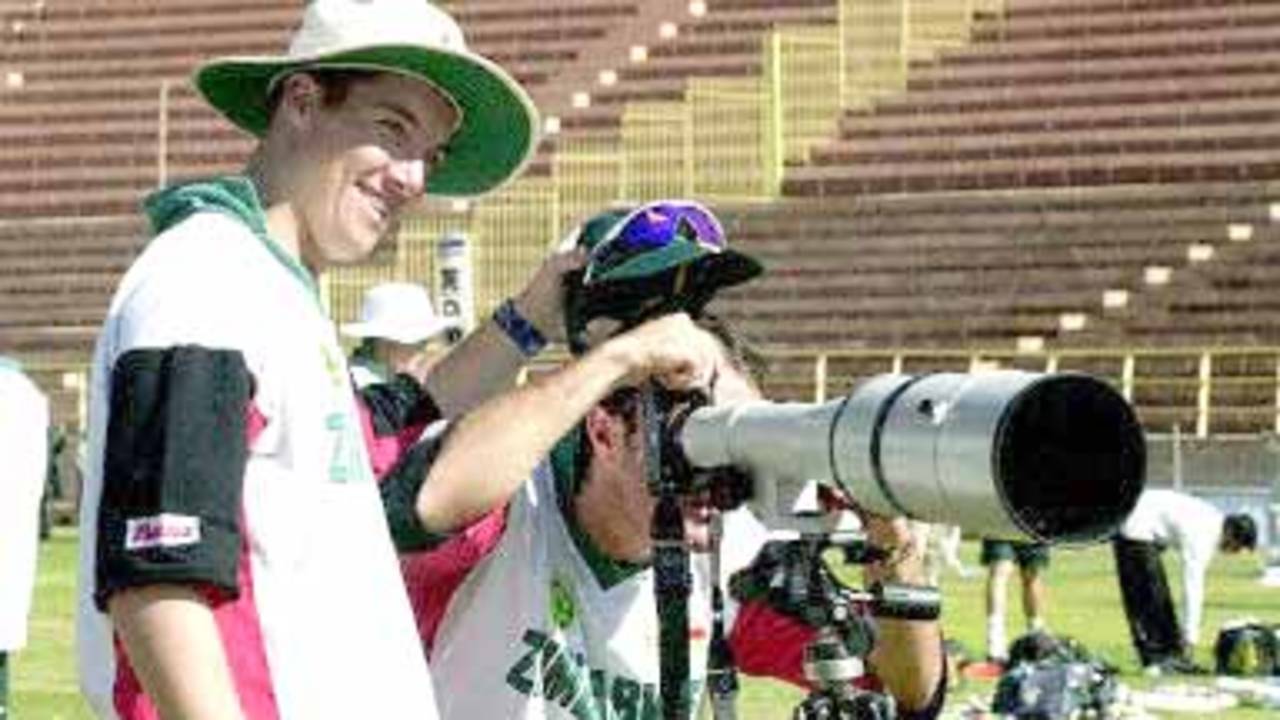 Zimbabwe cricketer Dirk Viljoen looks through a photographer's camera as his teammate Travis Friend (L) holds his cap during a practice session at Jodhpur cricket ground 07 December 2000, in Jodhpur. Zimbabwe will play its third one-day cricket match against India 08 December. India leads the series 2-0.